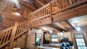 A wooden cabin interior with a kitchen area, wooden staircase, and a dining table.