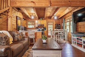 Interior de una cabaña de madera con sala de estar, cocina y comedor.