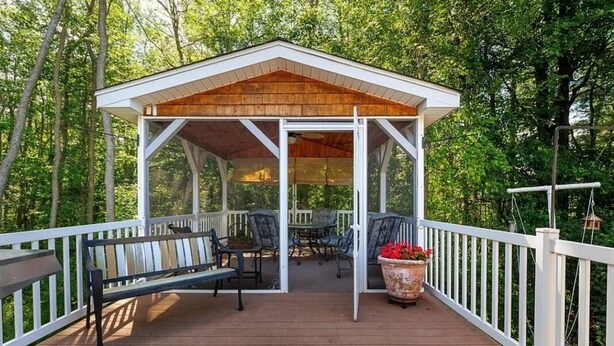 A covered outdoor deck with a wooden roof, white railings, and a bench. - Chippewa Bay Retreat (Hammond)