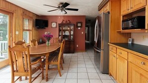 A kitchen with wooden cabinets, a dining table with chairs, a refrigerator, and a microwave. - Chippewa Bay Retreat (Hammond)