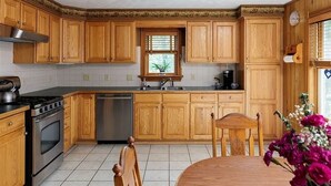A kitchen with wooden cabinets, a stove, a sink, and a window with blinds. - Chippewa Bay Retreat (Hammond)