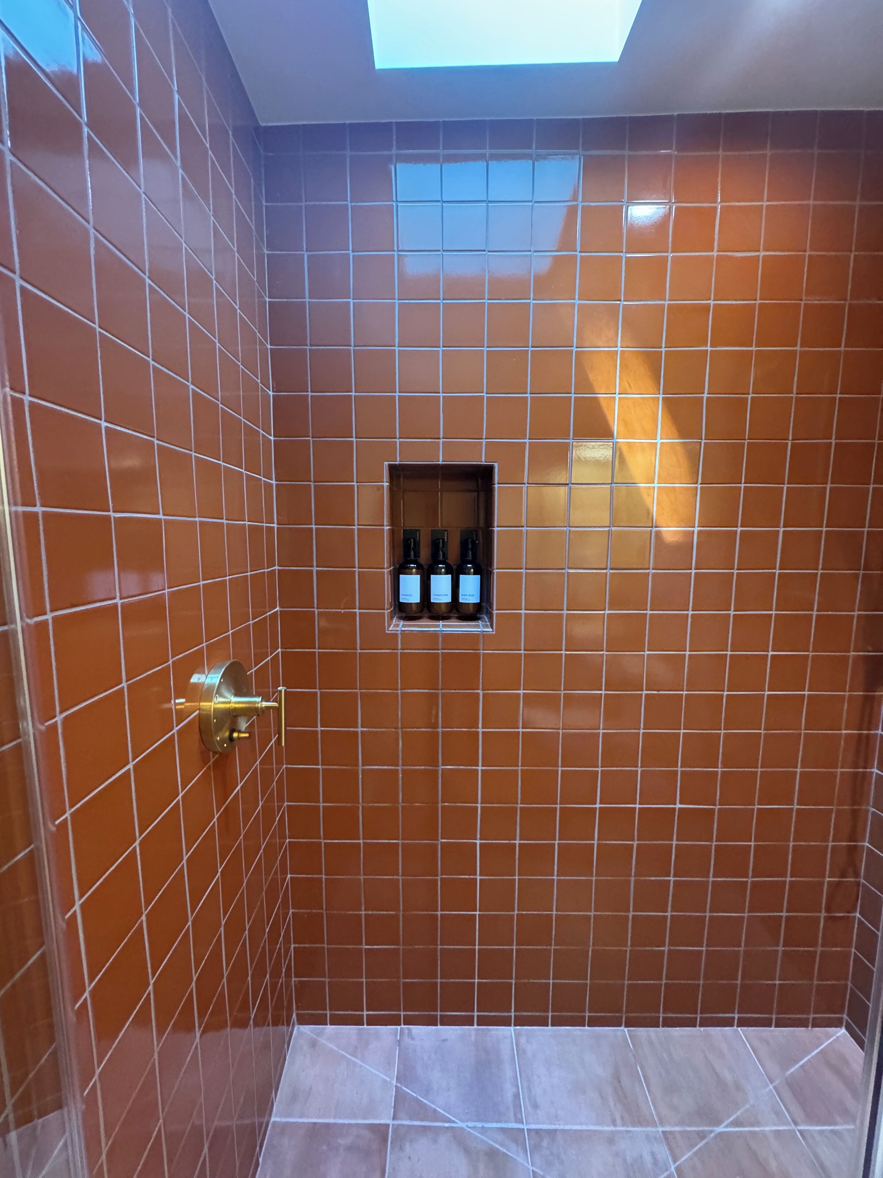 Een badkamer met bruine betegelde muren, een klein raam en een plank met flessen.