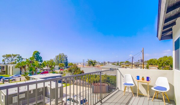 A balcony with a view of a residential area, a table with chairs, and a railing.