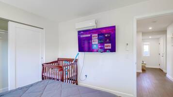 A bedroom with a bed, a crib, a mounted TV displaying streaming services, and a hallway leading to another room.