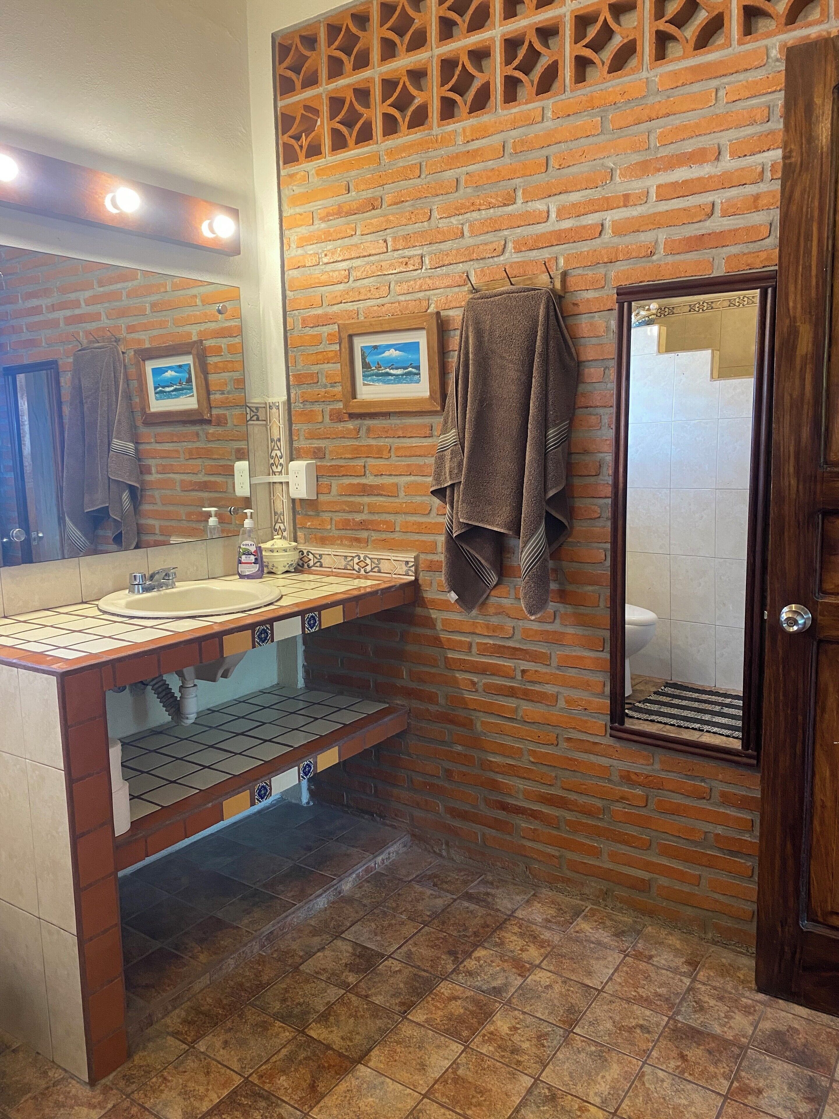 Un baño con pared de ladrillo, un lavamanos con espejo y un perchero para toallas.