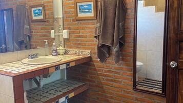 Un baño con pared de ladrillo, un lavamanos con espejo y un perchero para toallas.