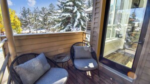 En balkong med två stolar och ett litet bord, med utsikt över ett snötäckt landskap med träd.