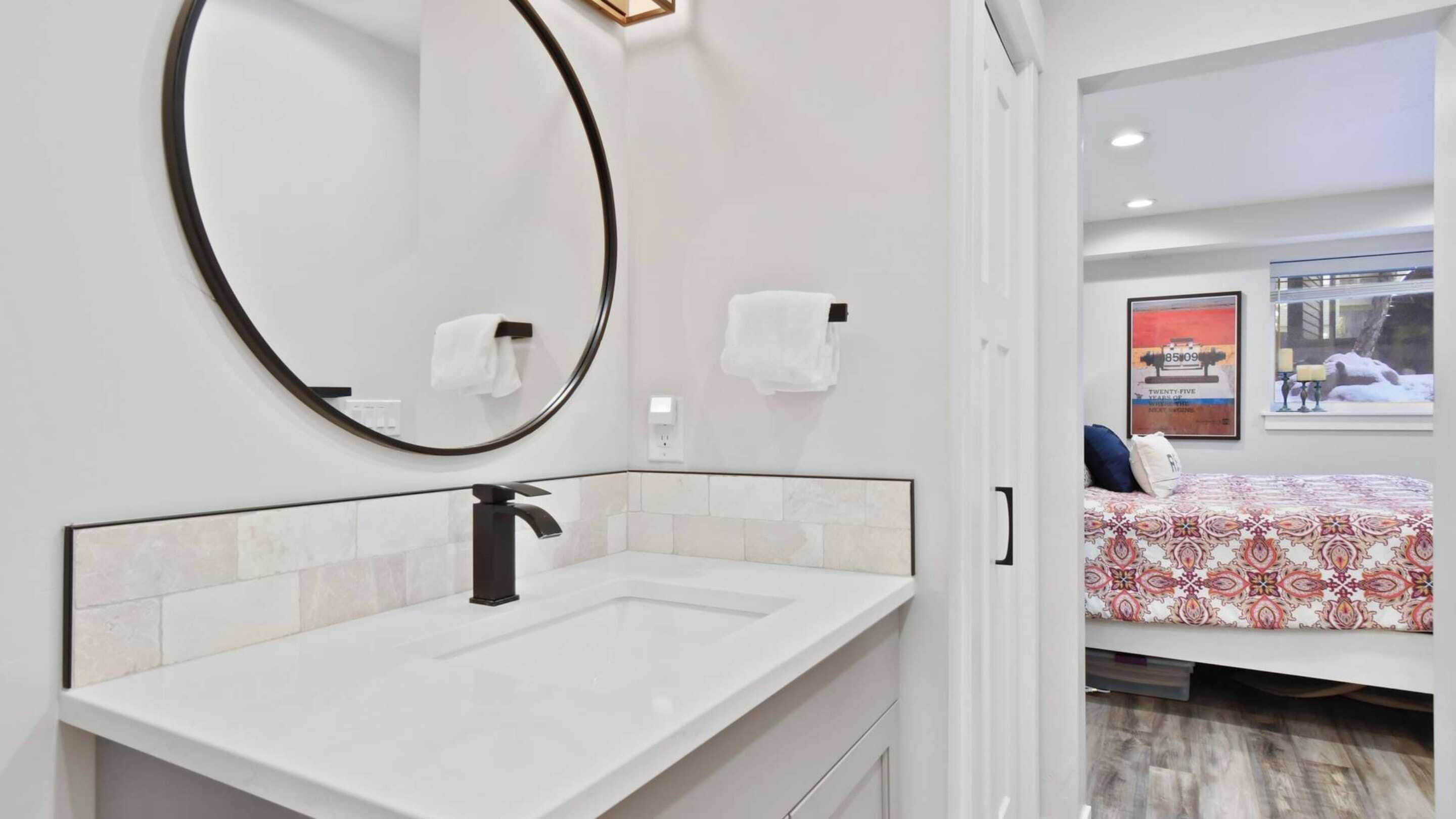 A modern bathroom with a white sink, a round mirror, and two white towel dispensers.