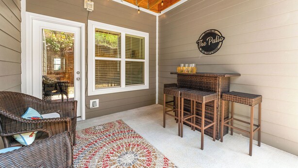 Un área de patio techada con mobiliario de mimbre, un tapete decorativo y un letrero en la pared.