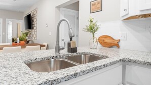 Una cocina moderna con encimeras de granito, lavamanos de acero inoxidable y armarios blancos.