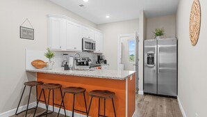 Una cocina moderna con armarios blancos, un refrigerador de acero inoxidable y una zona de bar con taburetes.