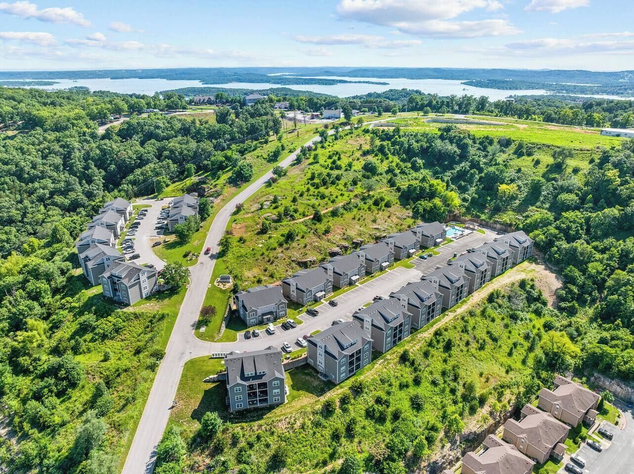A residential area with multiple two-story houses arranged in a semi-circular pattern, surrounded by lush greenery and a clear sky.