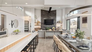 Uma cozinha moderna com uma ilha central, uma área de jantar com uma mesa comprida e uma televisão sobre a lareira.