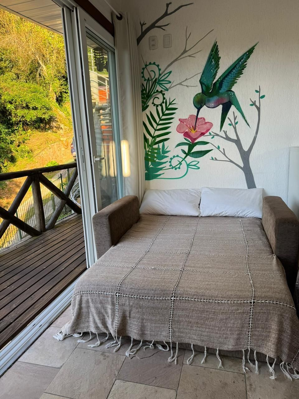 A bedroom with a bed, pillows, and a mural of a tree with a bird and flowers.