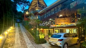 A hotel with a thatched-roof structure, a paved driveway, and a parked car. - Pousada Asa Delta Jurerê (Florianopolis)