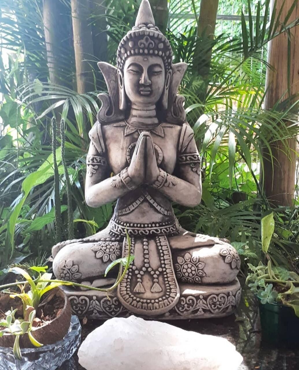 A seated statue with intricate patterns, surrounded by lush greenery.