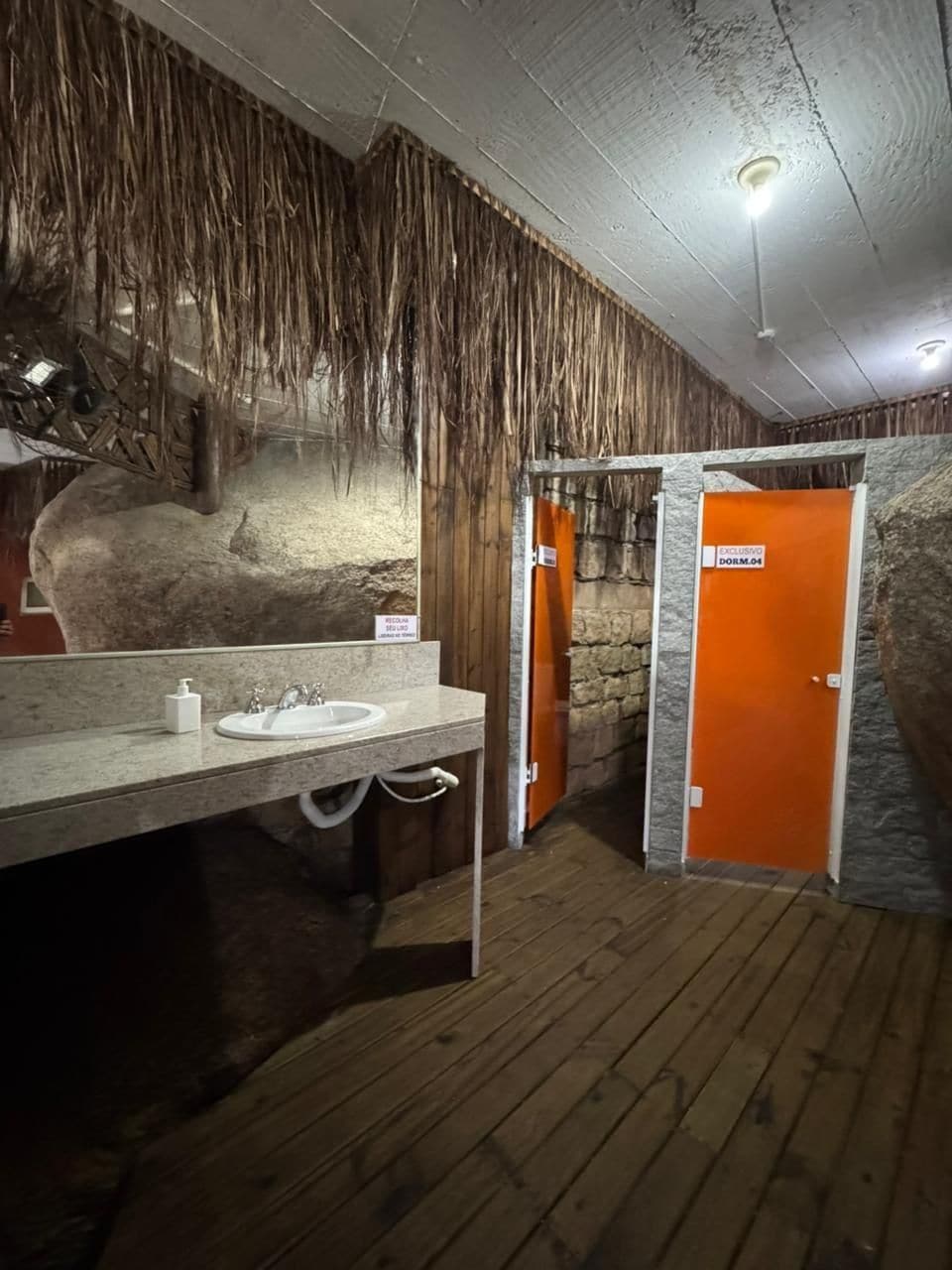 A rustic bathroom with a stone wall, a wooden floor, and a sink with a mirror.