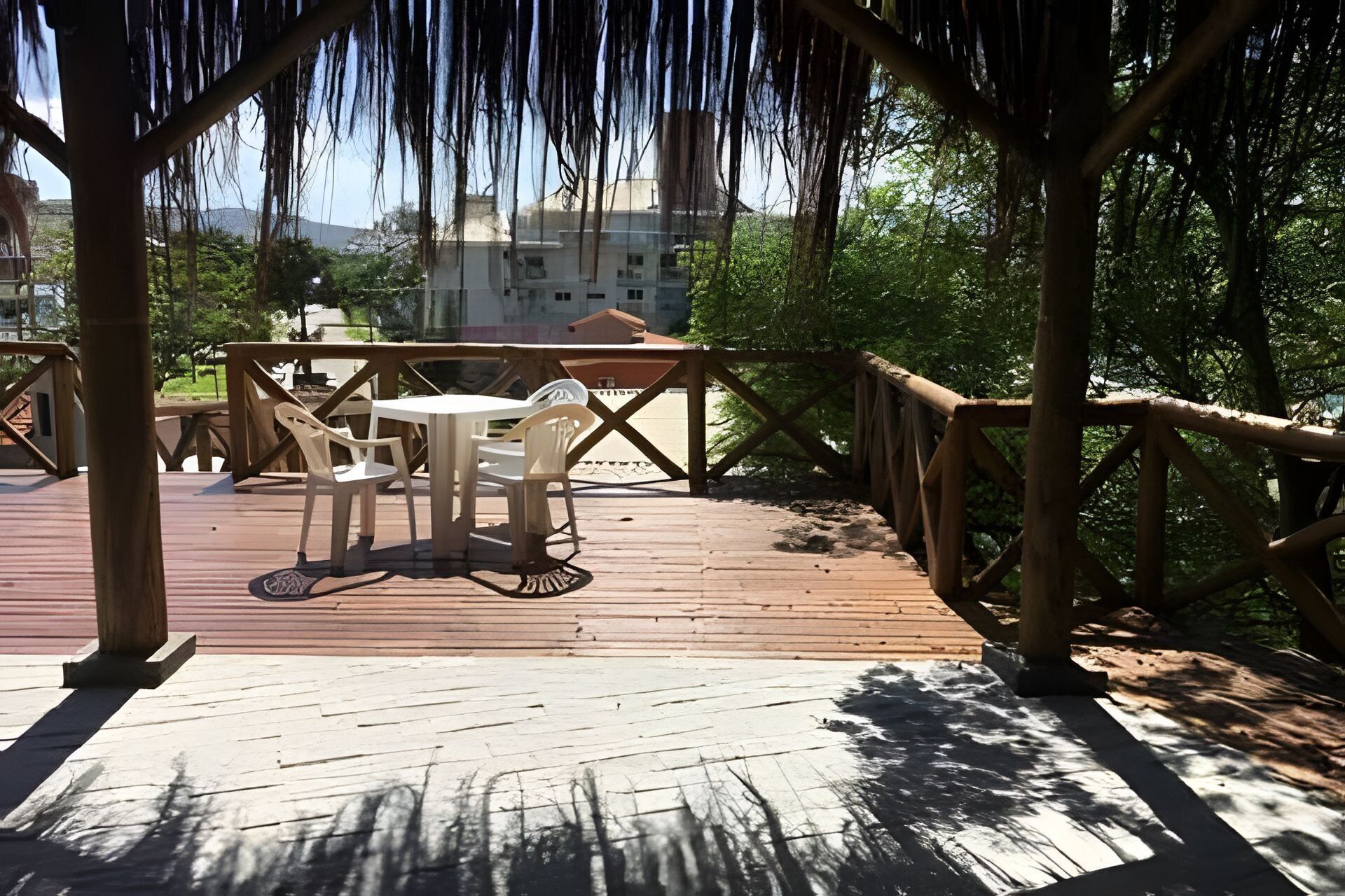 Een houten terras met een tafel en stoelen, omgeven door een houten leuning en bomen.