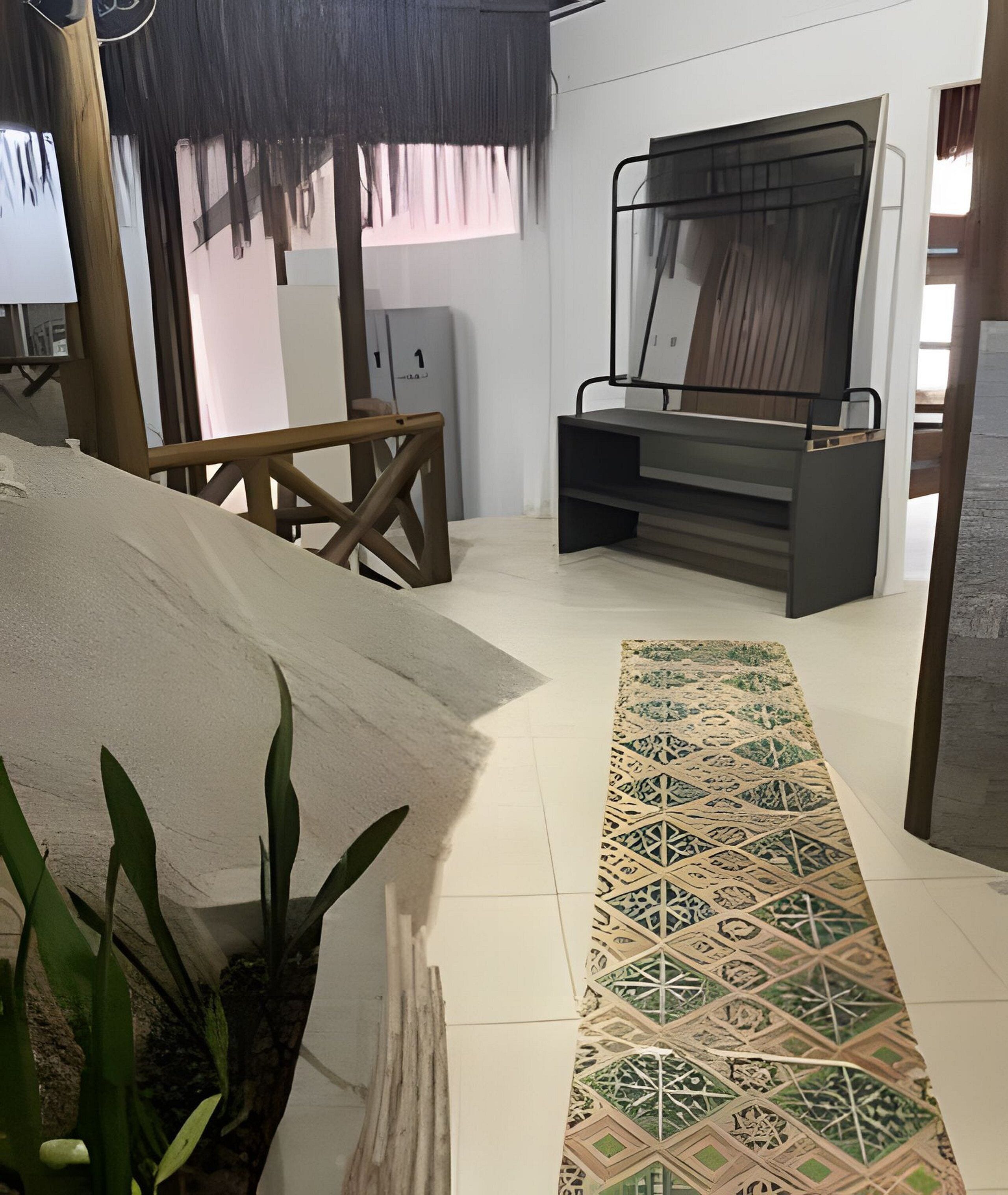 Una habitación con cama, escritorio, silla, planta y alfombra estampada.