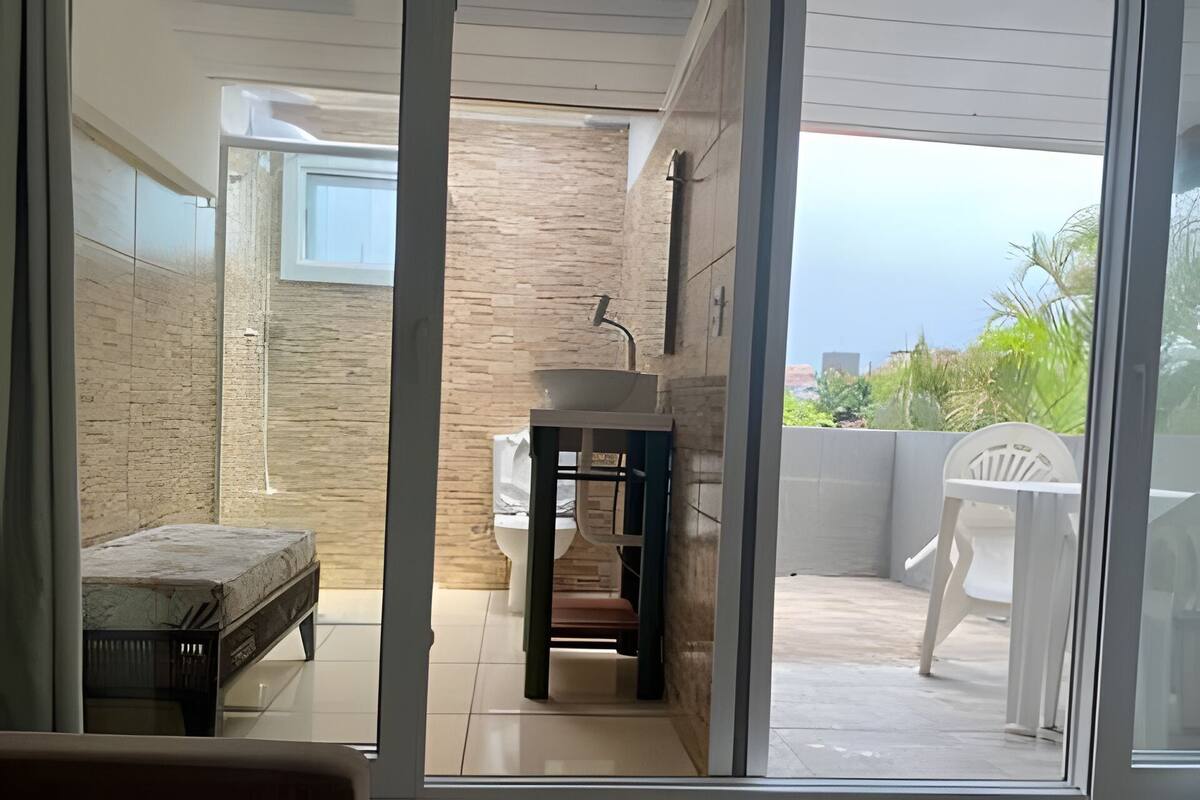 A modern bathroom with a stone sink and bench, a view of the outdoors, and a balcony with a chair.