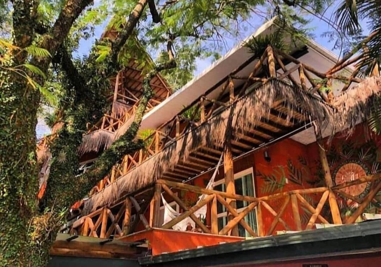 Una estructura con techo de paja y una escalera de madera que conduce a un edificio rojo.