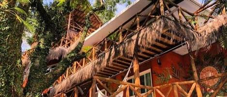 Una estructura con techo de paja y una escalera de madera que conduce a un edificio rojo.