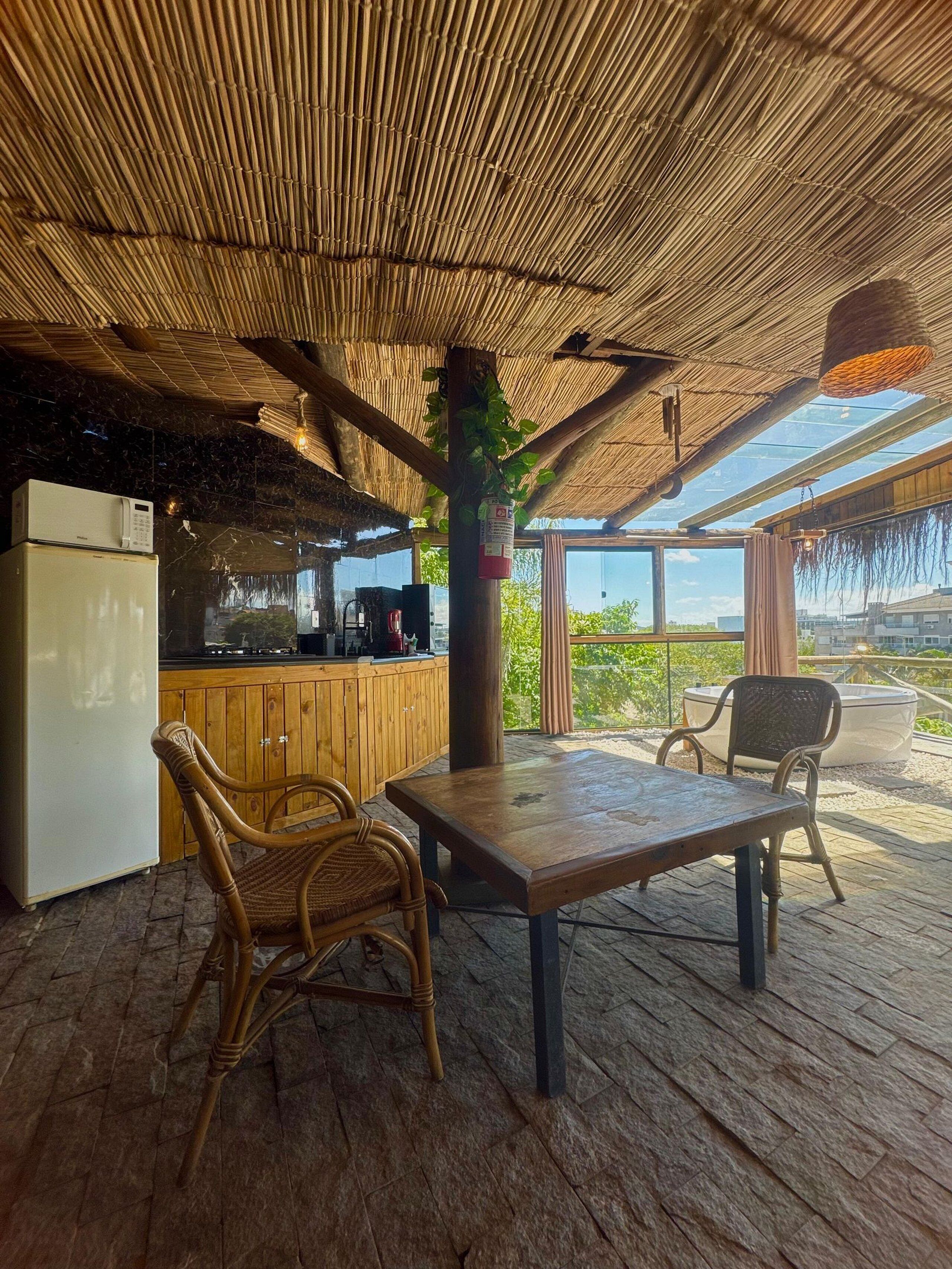 A covered outdoor dining area with a wooden table and chairs, a refrigerator, and a kitchen area with a stove and microwave.