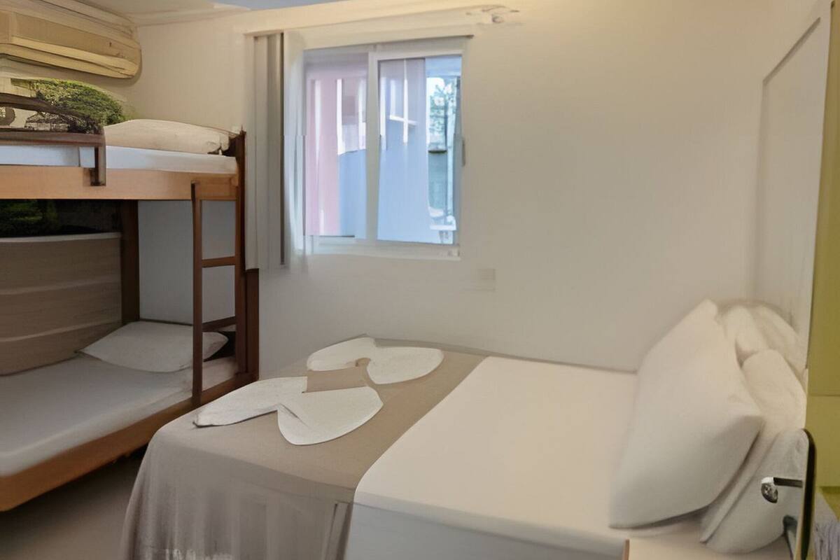 A compact bedroom with a bunk bed, a single bed, a small window, and a wooden floor.