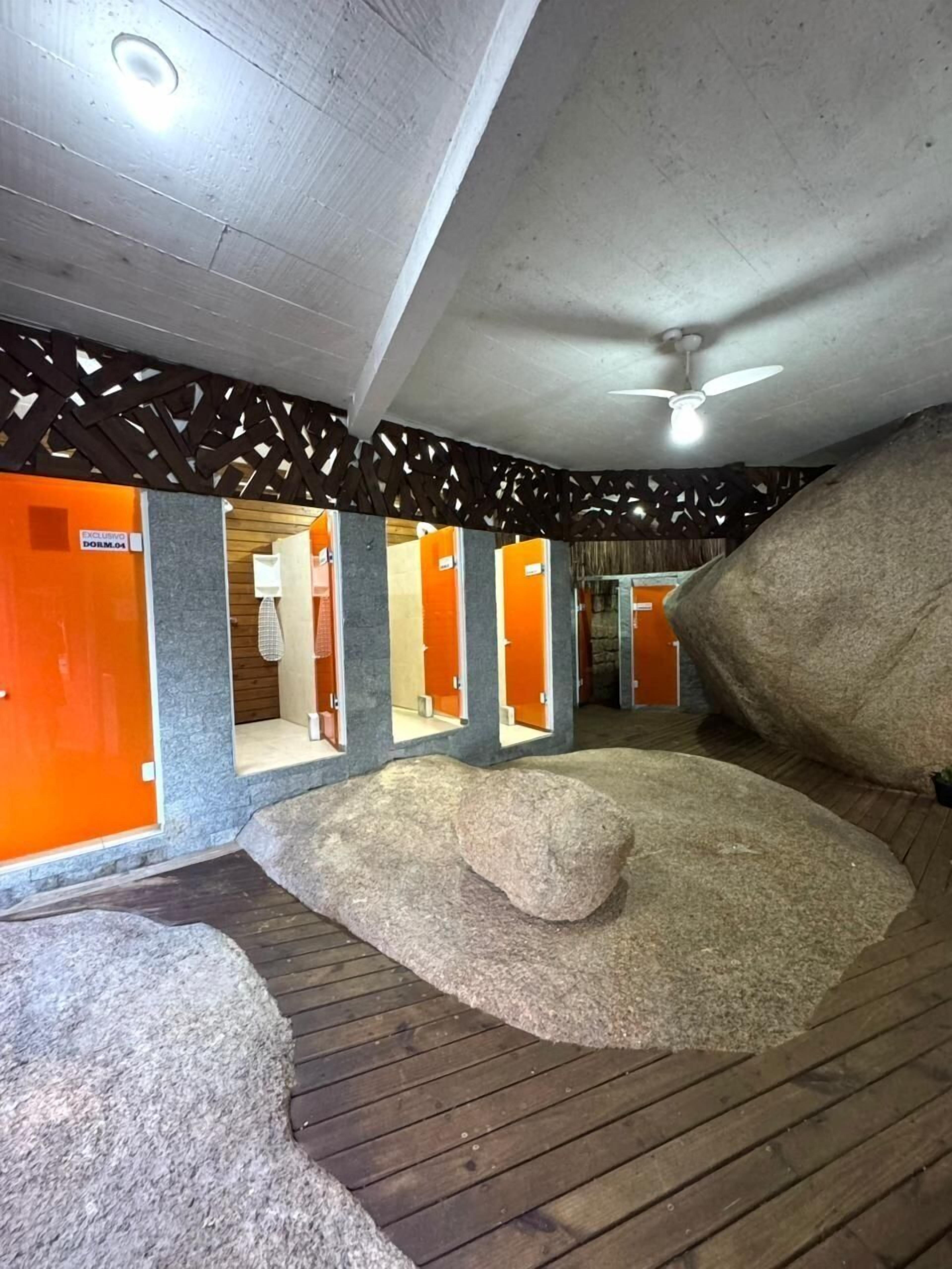 A hotel lobby with a modern design, featuring a large rock centerpiece, wooden flooring, and orange accent walls.