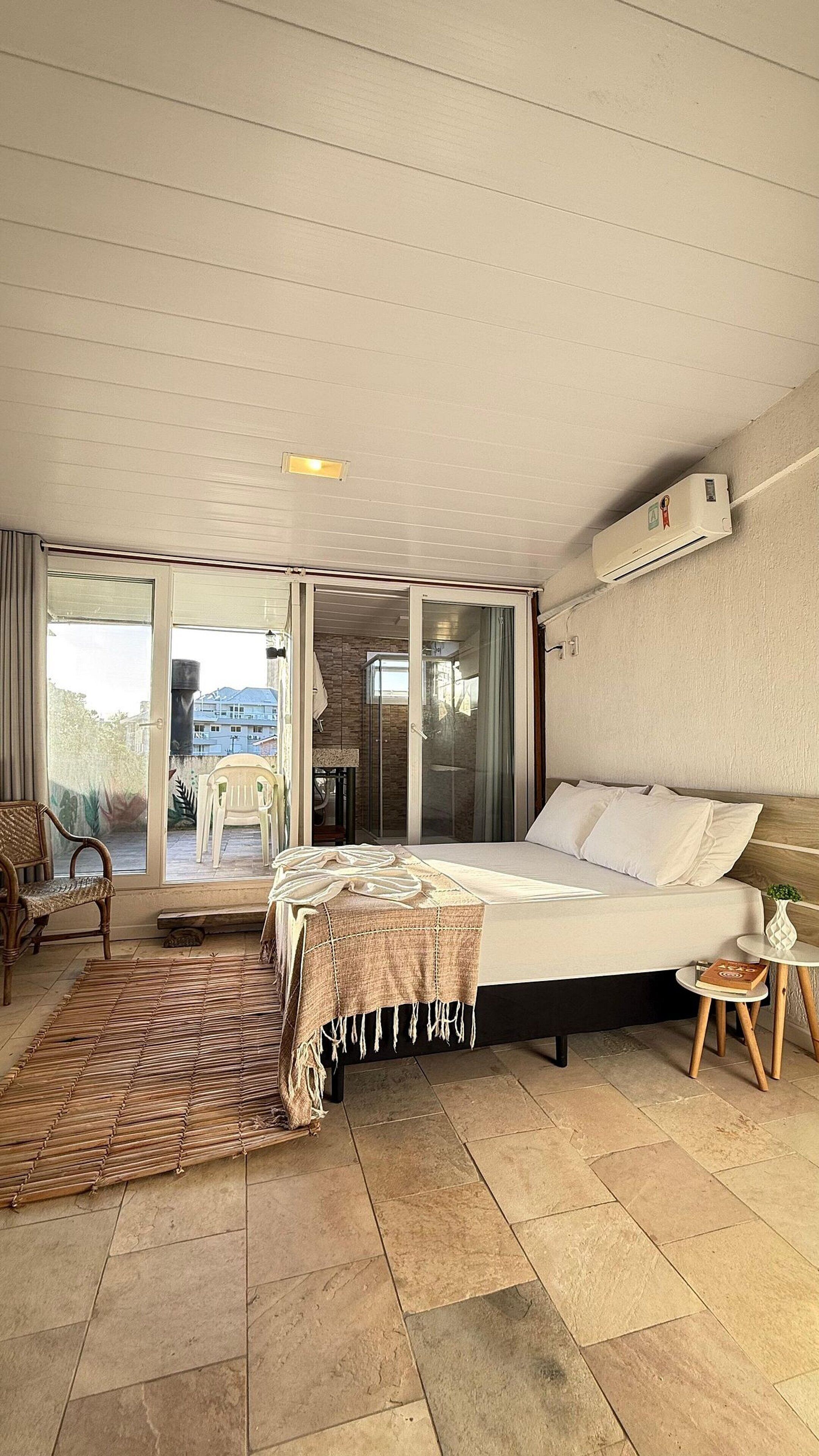 Een slaapkamer met een bed, een tafeltje, een stoel, een raam en een schuifdeur naar een buitenruimte.