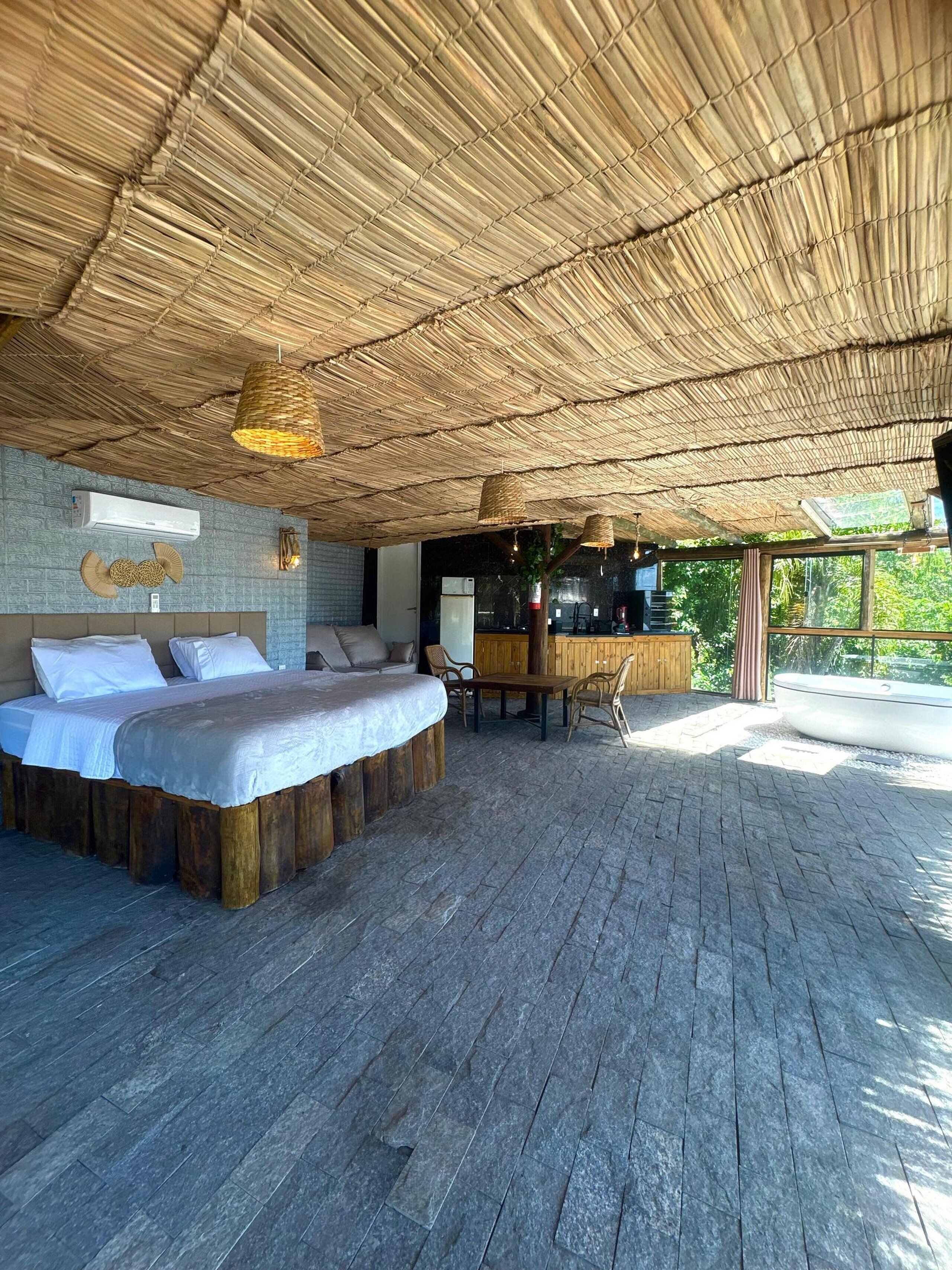 A spacious room with a large bed, a wooden table, and a thatched ceiling.