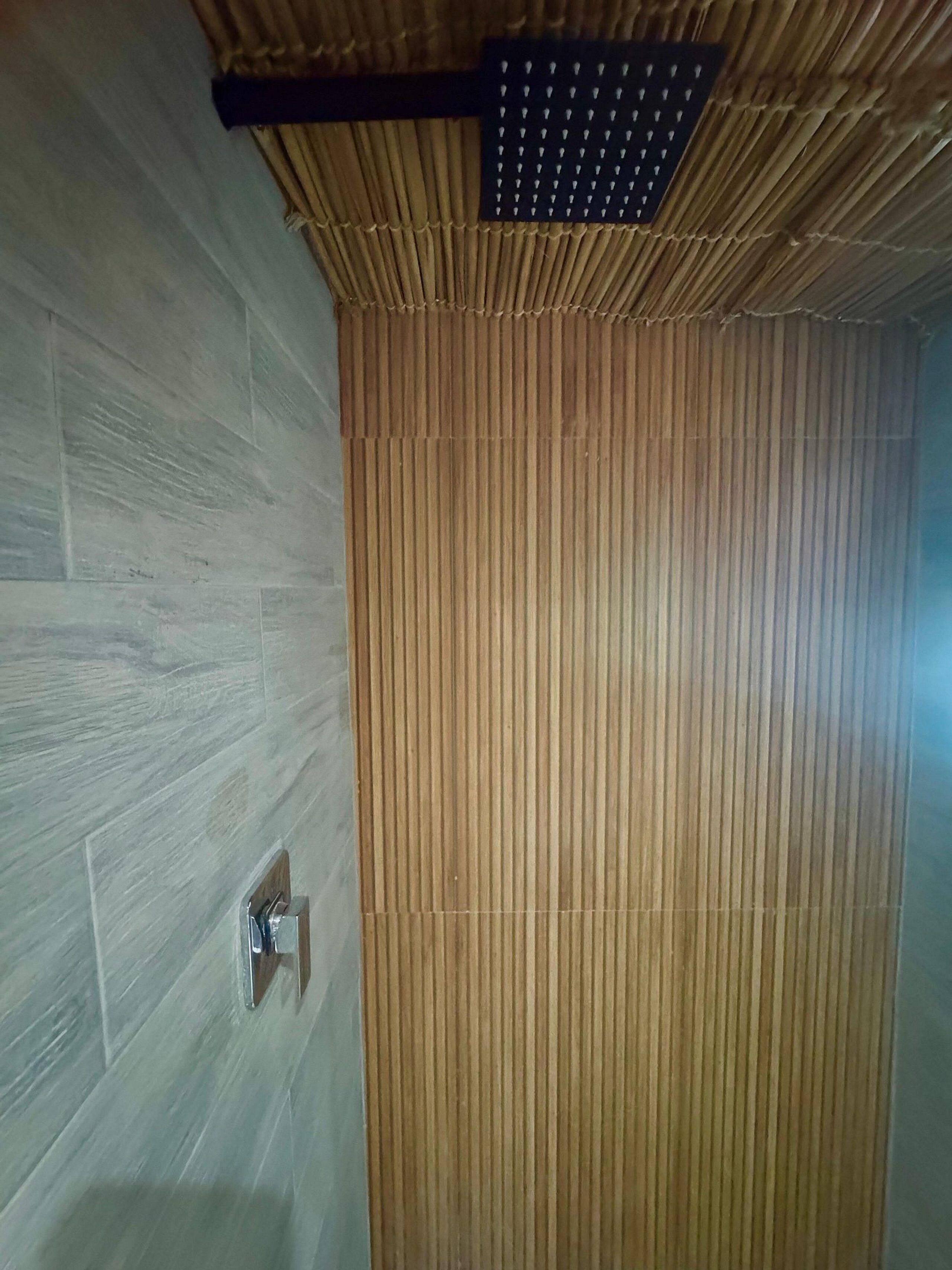 A bathroom with a bamboo panel wall and a shower area with a ceiling-mounted rain showerhead.