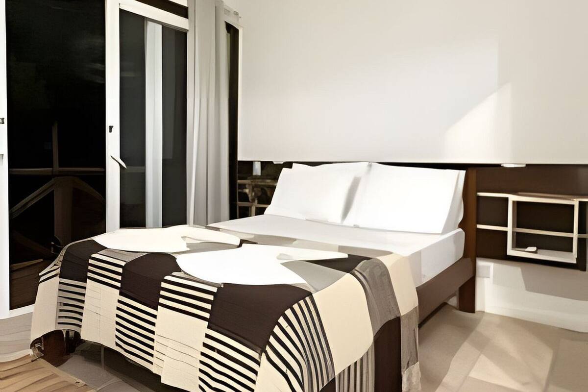 A modern bedroom with a large bed, a wooden floor, and a sliding glass door leading to an outdoor area.