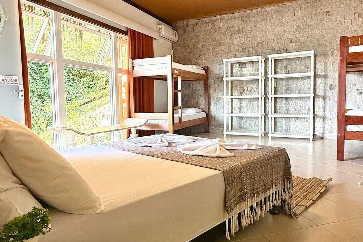 A room with bunk beds, a small table with a book, and a view of greenery outside.