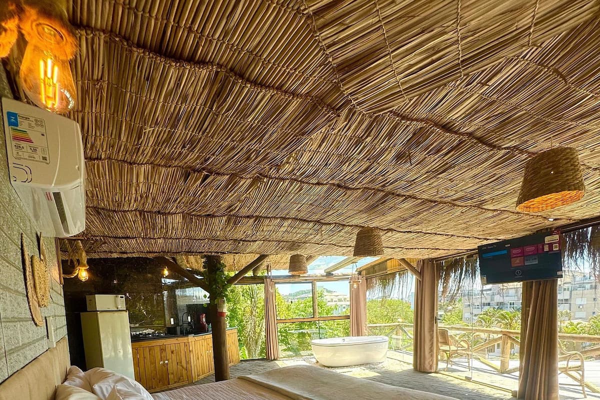 A room with a bed, a wooden bench, a table, and a thatched roof.