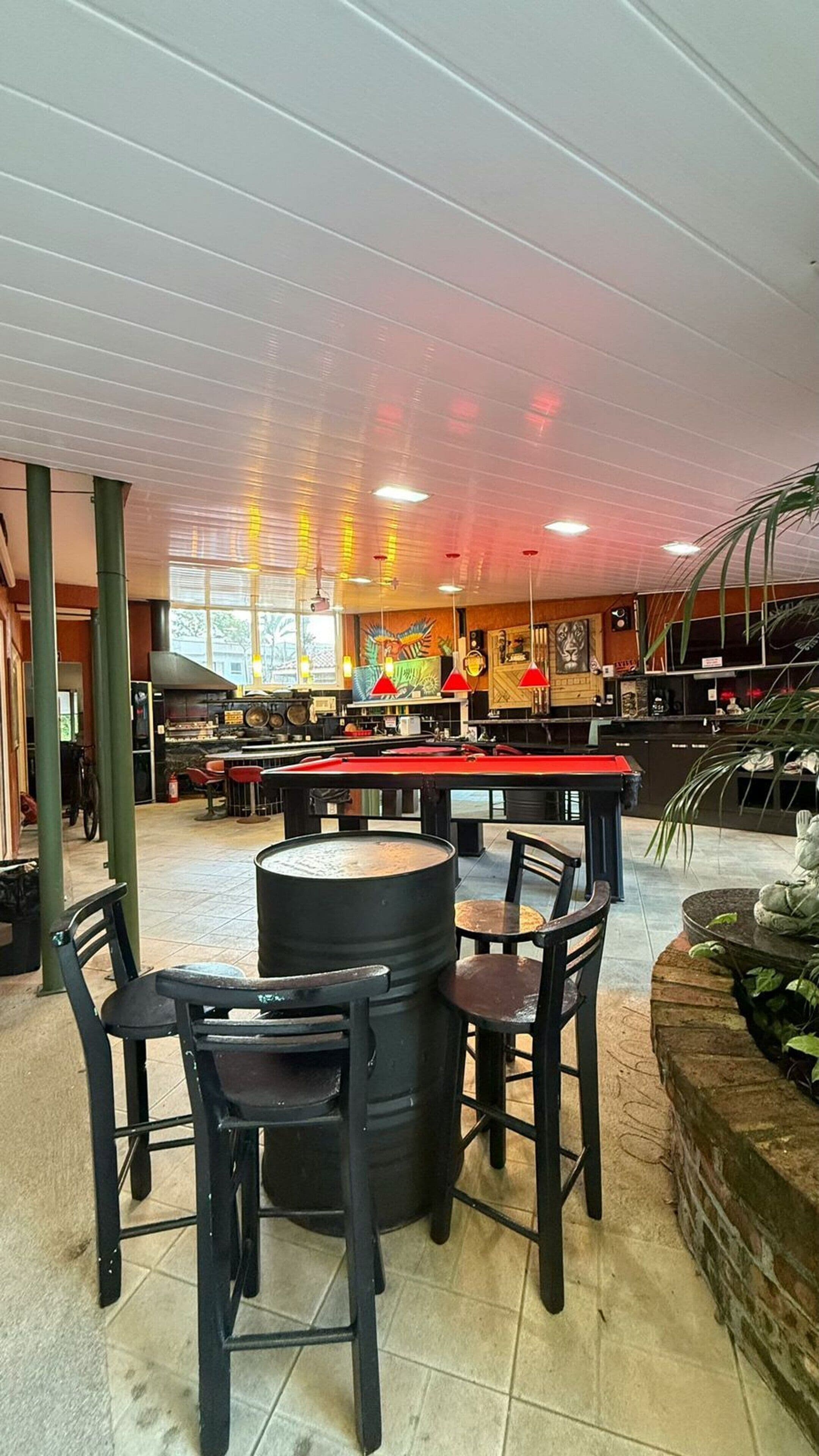 A spacious indoor area with high ceilings, a pool table, and several tables and chairs.