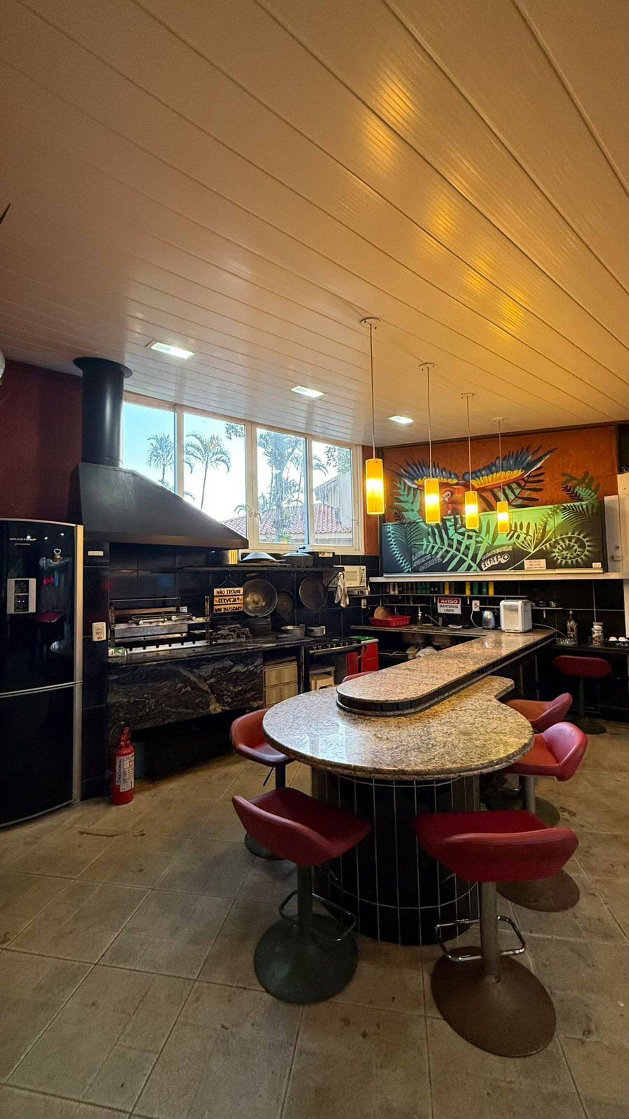 A restaurant with a central island bar, red bar stools, a large mural on the back wall, and a kitchen area with a stove and pots.