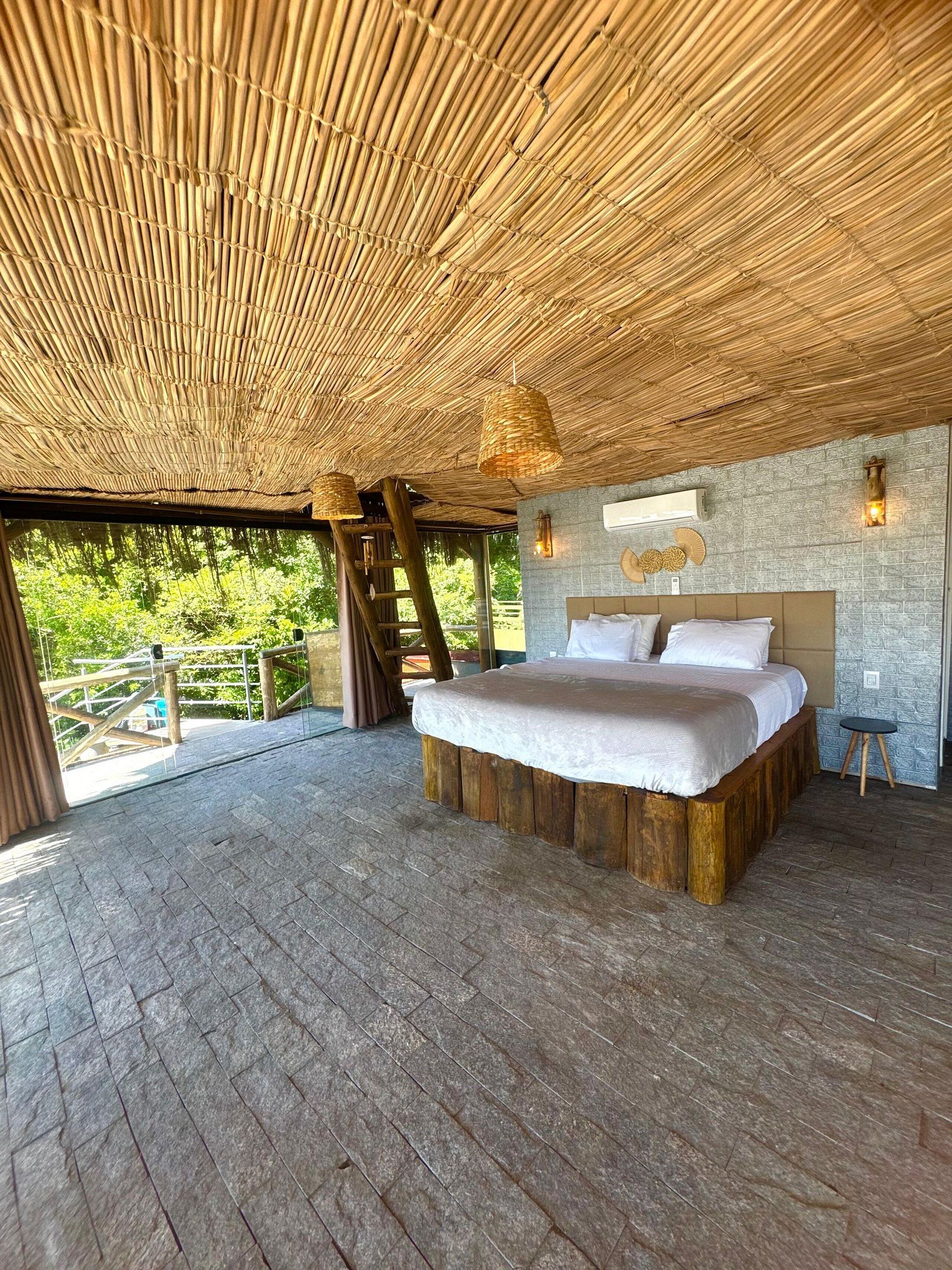 A spacious bedroom with a large bed, a stone wall, and a wooden ceiling.