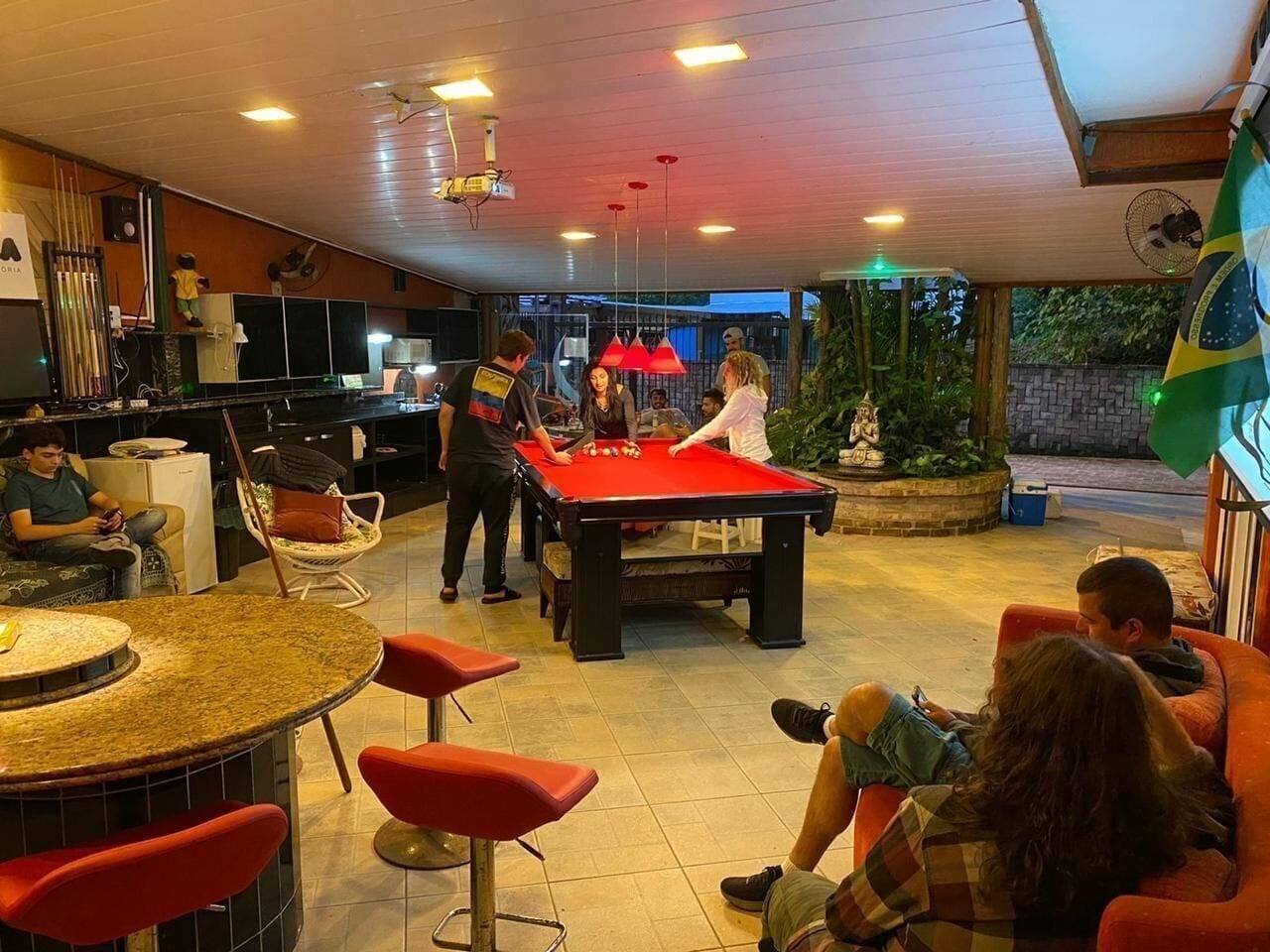 Una mesa de billar en una sala con zona de bar, sillas y una estatua.