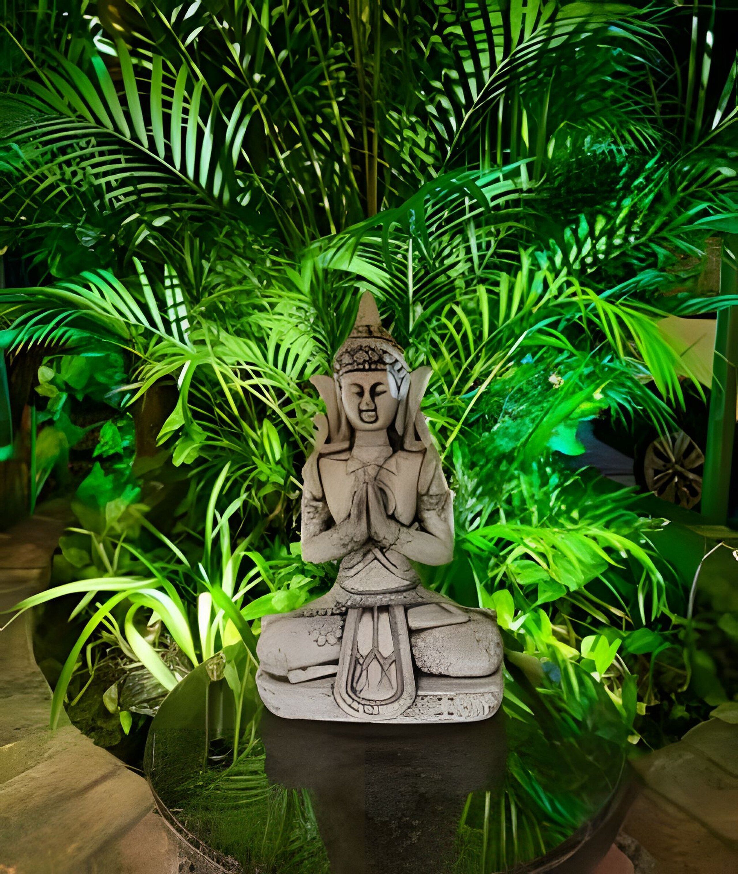 A statue of a seated figure in a meditative pose, surrounded by lush green foliage.