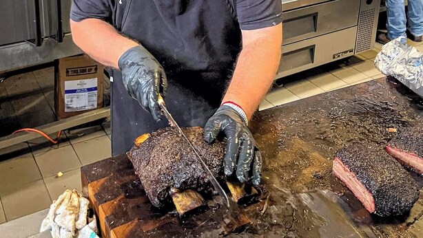 Une personne est en train de découper une grande pièce de viande sur une planche à découper dans une cuisine.