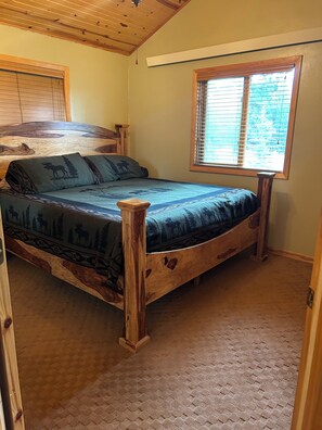 Une chambre à coucher avec un lit en bois, une tête de lit, une fenêtre avec des stores et un sol recouvert de moquette.