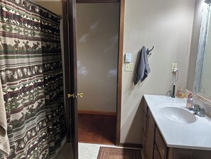 Une salle de bain avec un lavabo blanc, un miroir, un porte-serviettes et une porte donnant sur une pièce décorée de rideaux à motifs.