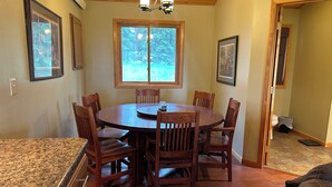 A dining area with a wooden table and chairs, a window with a view of trees, and a ceiling light fixture. - Adventure Awaits 16 Private Acres secluded getaway in the beautiful Black Hills (Lead)