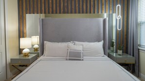 A modern hotel room with a large bed, a nightstand with a lamp, a mirror, and a potted plant. - Spectacular 9BR Villa Your Dream (Kissimmee)