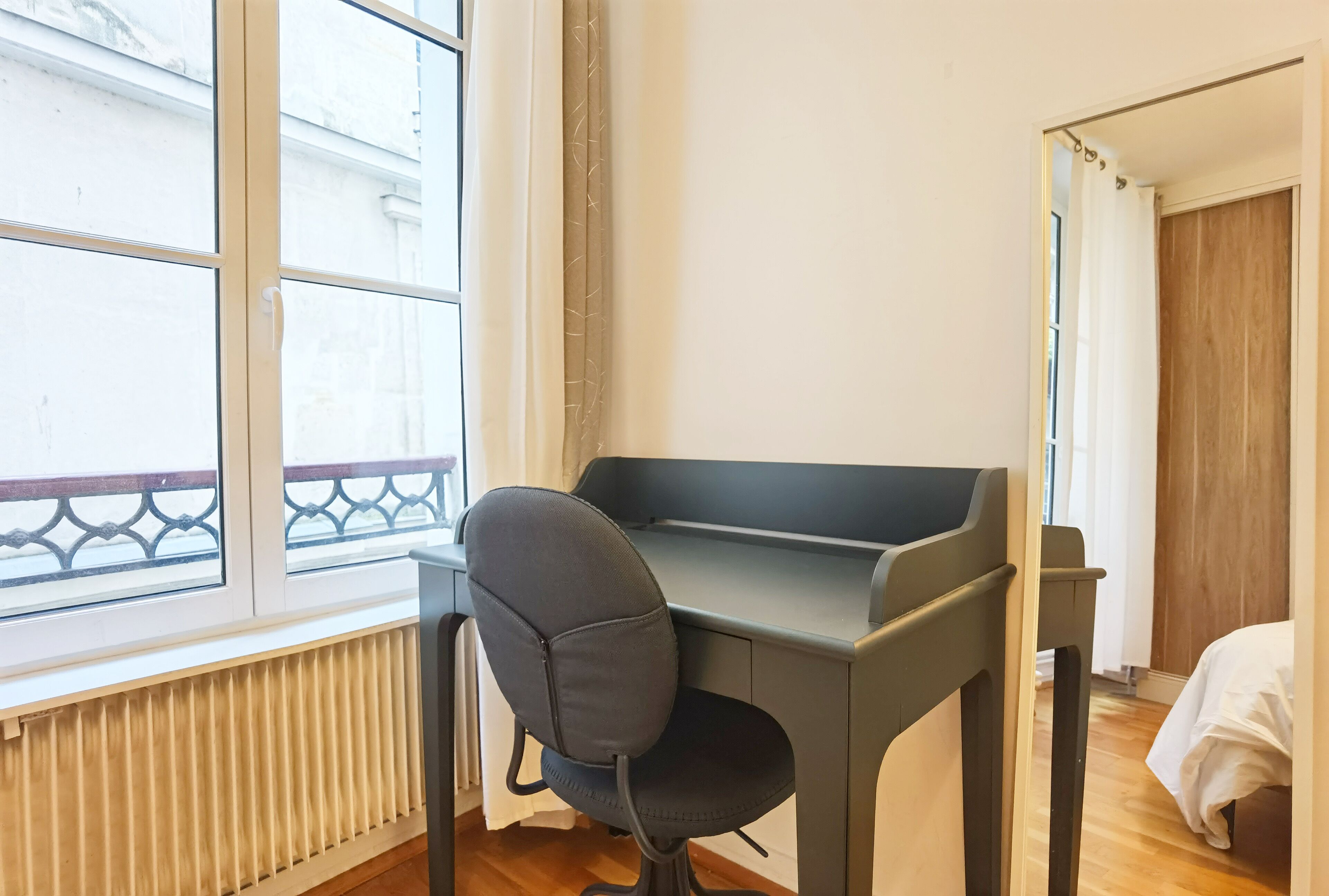 Una habitación con escritorio, silla, radiador, ventana y cama.