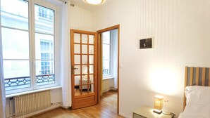 A bedroom with a wooden door, a bedside lamp, and a view through a window. - Calm apt /60m2/near Notre-Dame and Seine/2bdrs (Paris)