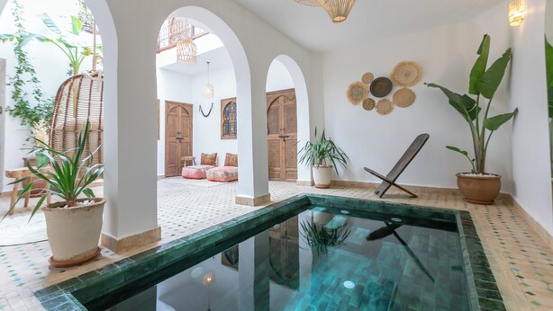 A pool area with a glass barrier, potted plants, and wooden doors in the background. - Riad Lamalika (Marrakech)