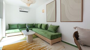 A modern living room with a green sectional sofa, a round coffee table, and a wicker chair. - Riad Lamalika (Marrakech)