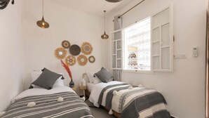 A room with two beds, a window with decorative curtains, wall art, and a thermostat. - Riad Lamalika (Marrakech)